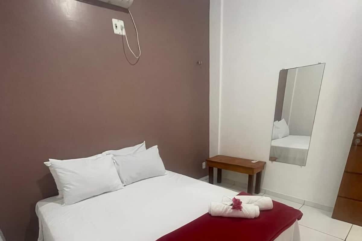 Una camera d'albergo con un letto, una coperta rossa, un tavolino, uno specchio e un condizionatore d'aria.