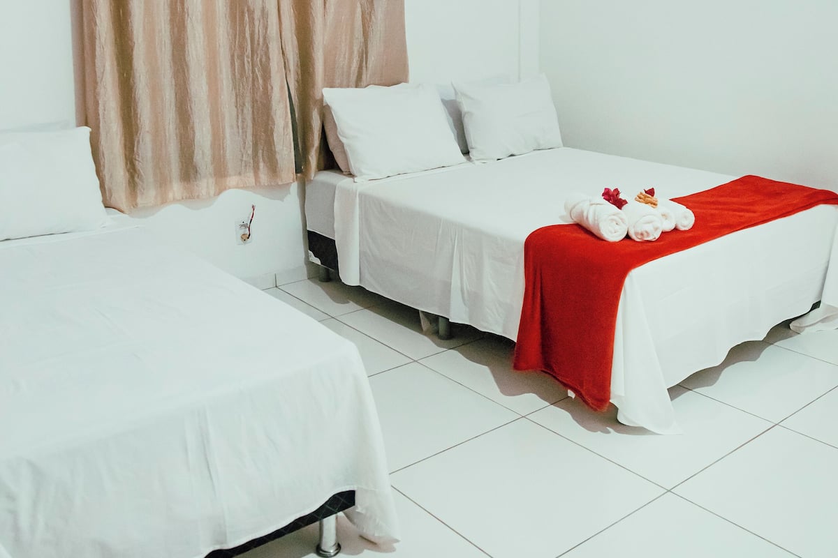 Camera d'albergo con due letti singoli, biancheria da letto bianca, una coperta rossa su un letto e un condizionatore d'aria a parete.