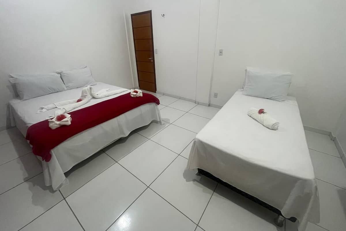 Due letti singoli con lenzuola bianche e coperte rosse, una porta di legno e pavimento piastrellato bianco.