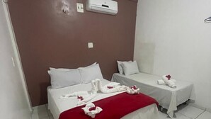 Ein Hotelzimmer mit zwei Betten, eine rote Decke auf dem größeren Bett und weiße Handtücher mit roten Blumen.