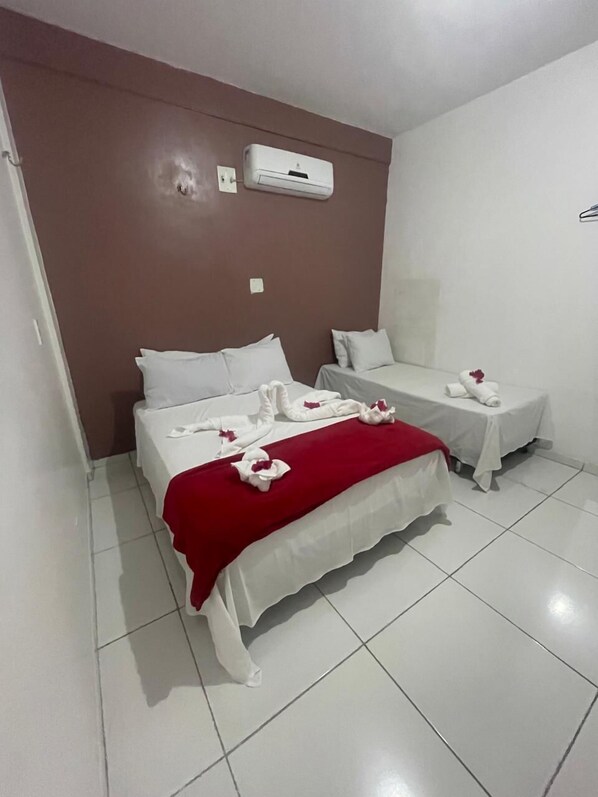Ein Hotelzimmer mit zwei Betten, eine rote Decke auf dem größeren Bett und weiße Handtücher mit roten Blumen.