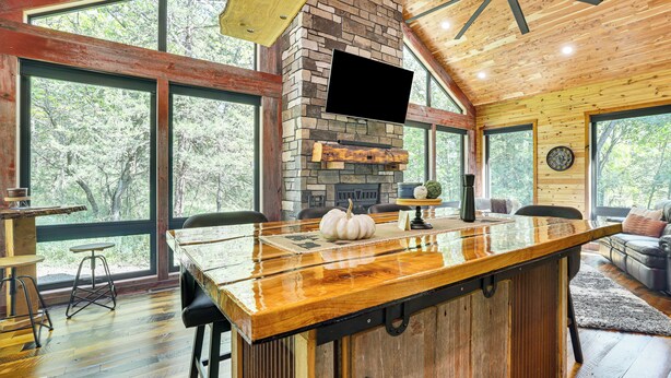 A spacious kitchen with a large island, stone fireplace, and large windows offering a view of the outdoors. - Galena Cabin on 20 Acres: 5 Mi to Downtown! (Galena)