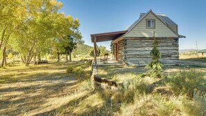 A rustic log cabin with a porch, surrounded by trees and a clear sky. - Bryce Canyon Basecamp: Historic Homesteader Cabin (Panguitch)