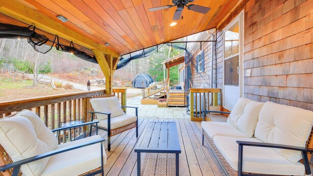 Um deck de madeira coberto com mobiliário de exterior, um ventilador de teto e vista para o quintal.