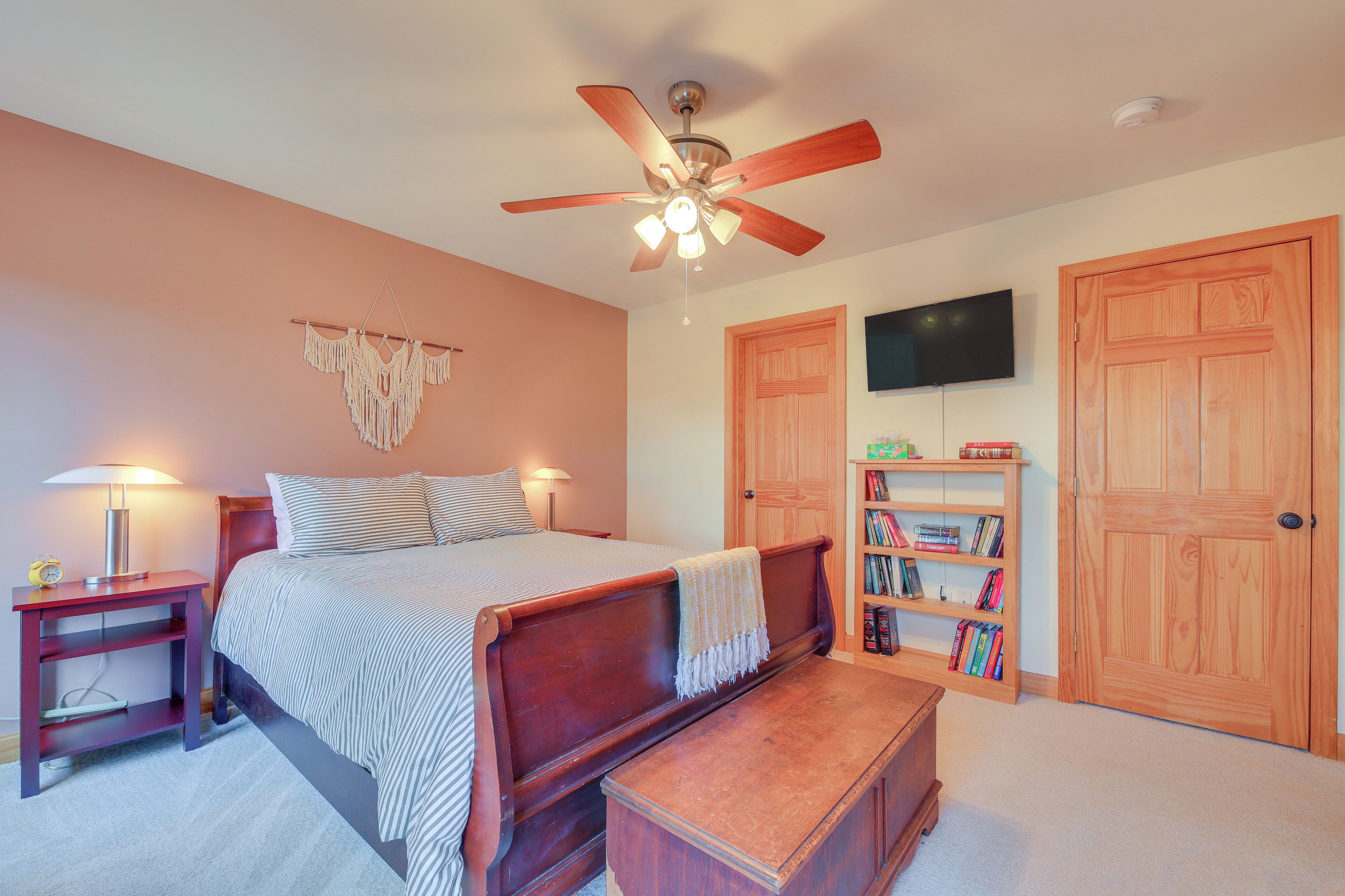 Une chambre à coucher comprenant un lit, des tables de chevet, un ventilateur de plafond, une bibliothèque et un téléviseur fixé au mur.
