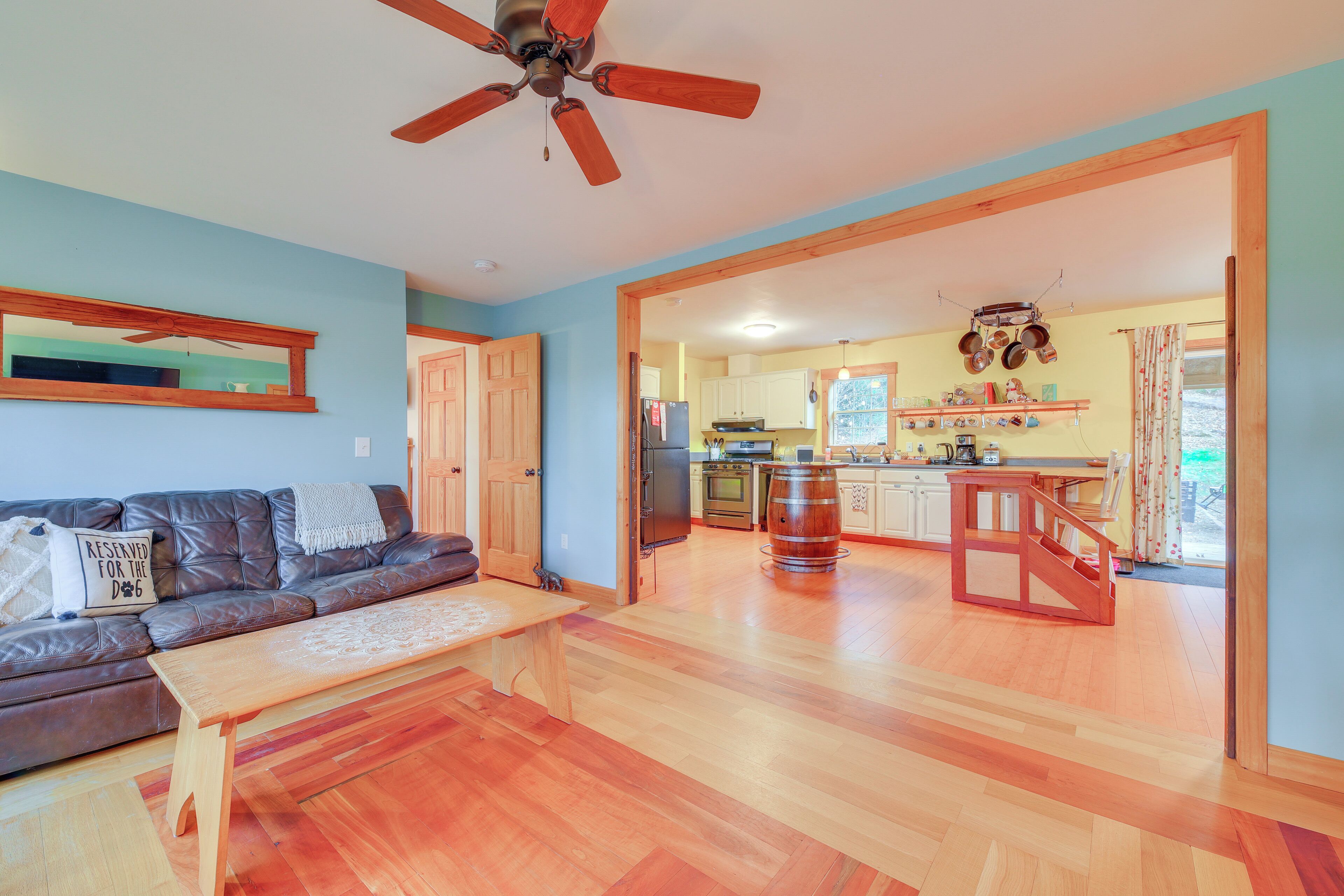 A spacious living room with a wooden floor, a leather sofa, a coffee table, and a ceiling fan.
