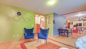Uma sala espaçosa com um sofá grande, duas poltronas azuis, uma mesa de jantar com cadeiras e uma cozinha ao fundo.