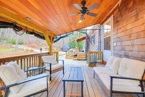Une terrasse en bois couverte, dotée de meubles d’extérieur, d’un ventilateur de plafond et offrant une vue sur le jardin arrière.