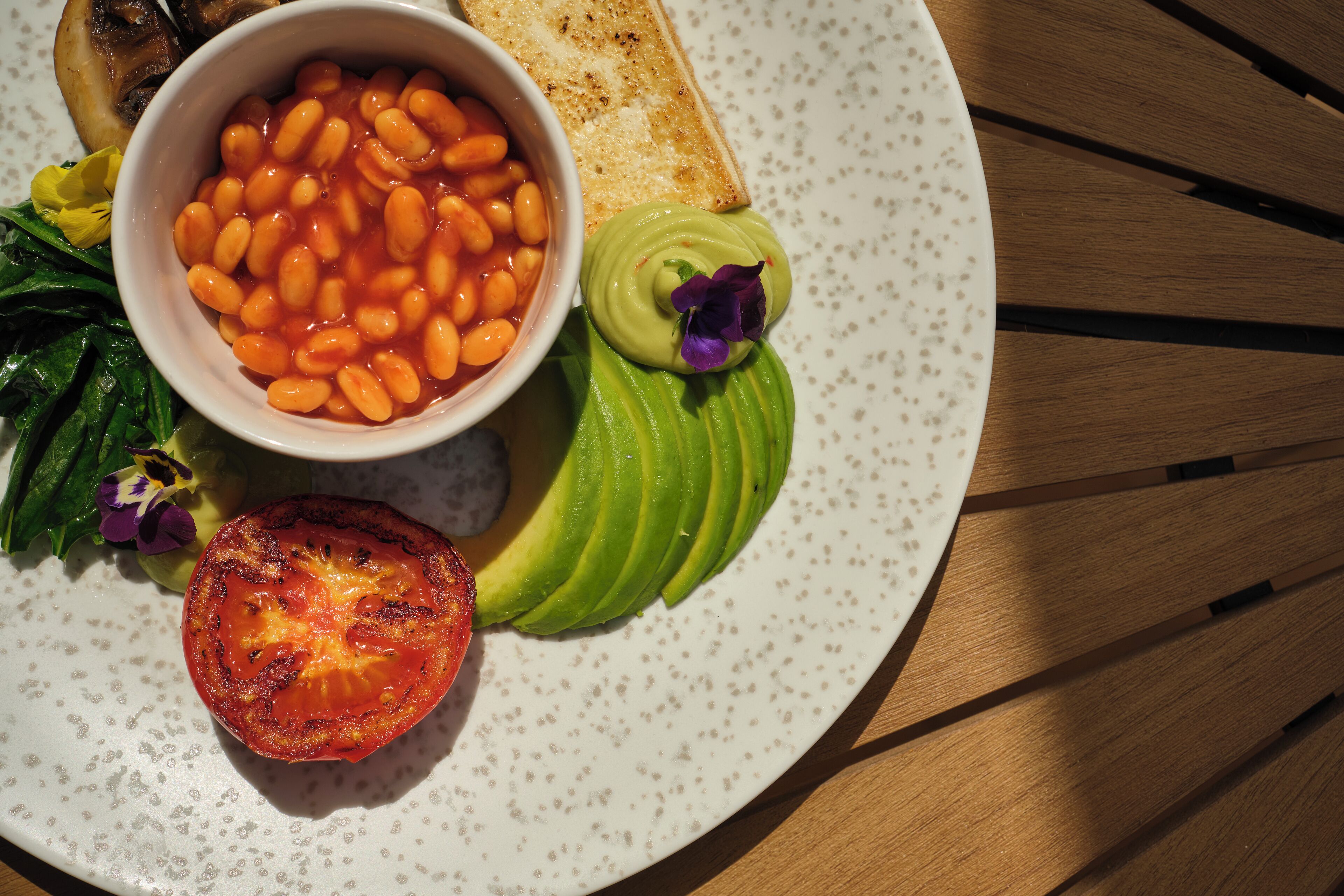 Un plato con frijoles, aguacate, tomate y vegetales verdes.