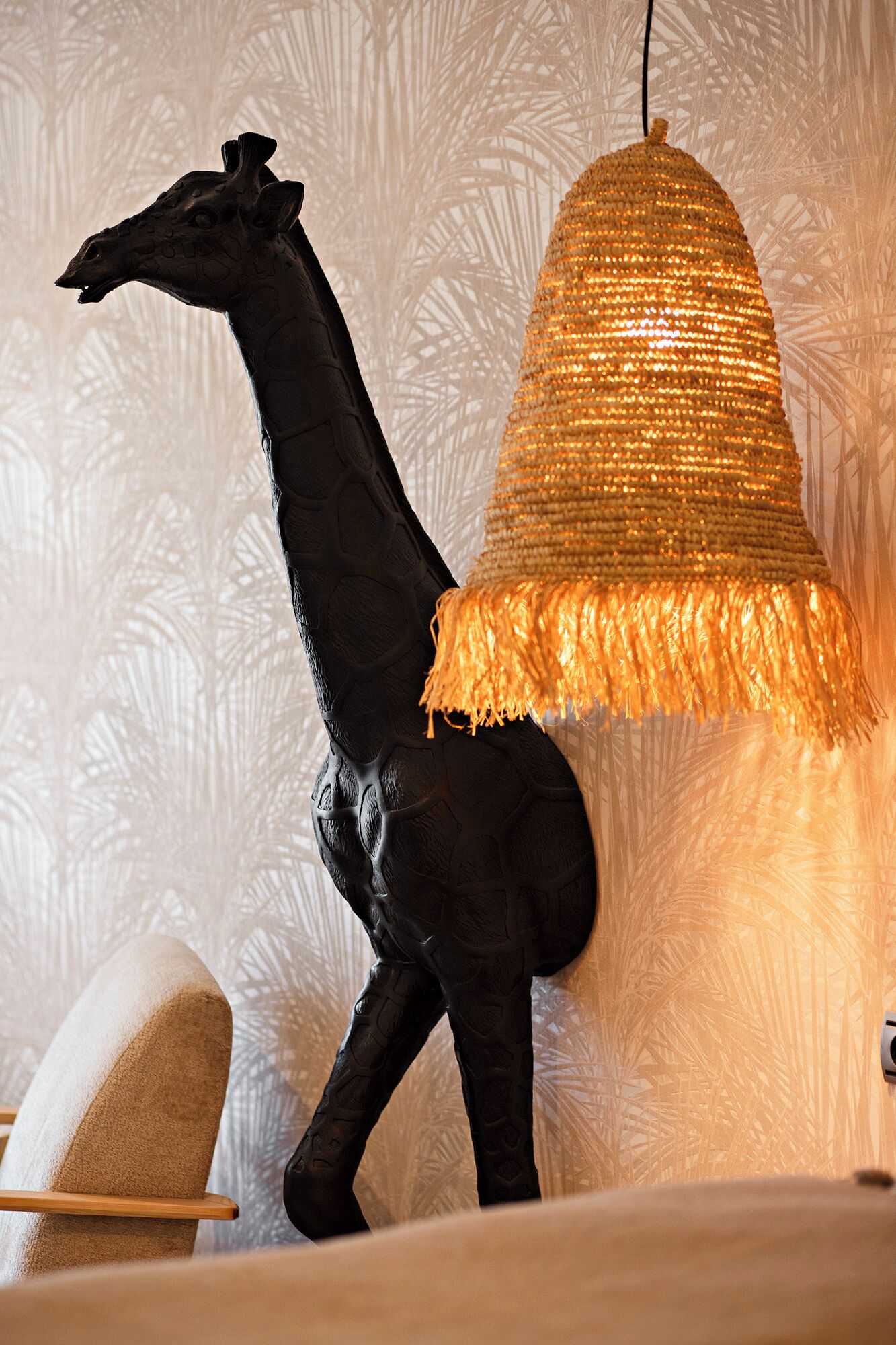 Een girafbeeld naast een structuurwand en een hanglamp.