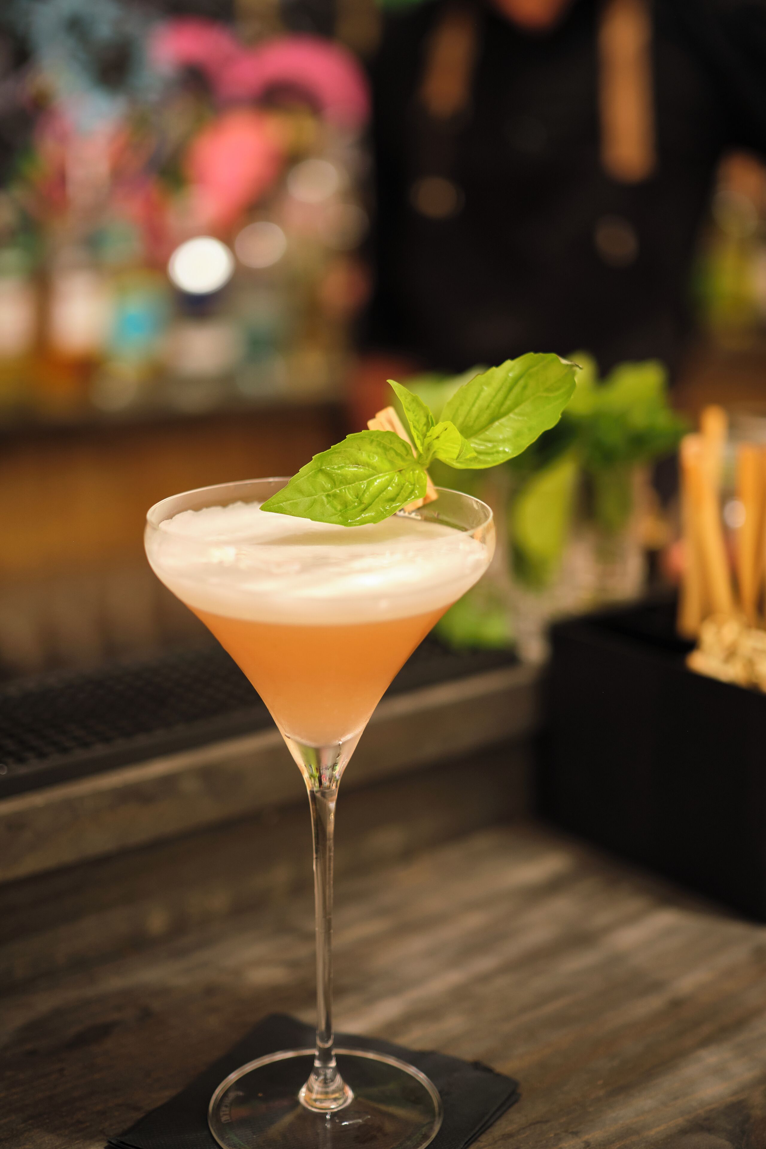 Un cóctel en una copa de martini con una guarnición, sobre una barra de madera.