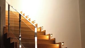 A modern staircase with wooden steps and glass railings, illuminated by wall-mounted lights. - ALCAIDESA BOUTIQUE HOTEL (La Línea de la Concepción)