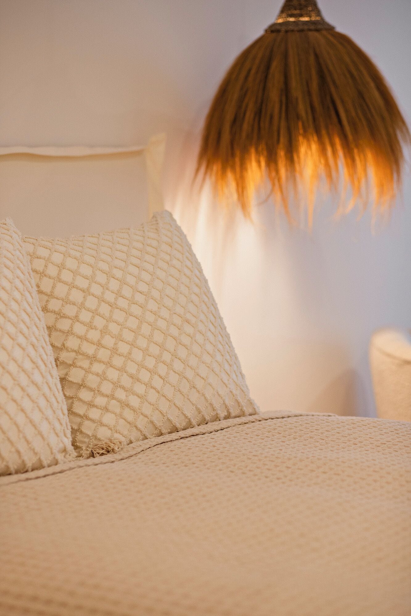 Una cama con cubrecolcha blanco texturizado y dos almohadas.