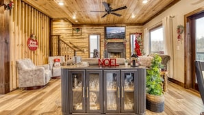 A cozy log cabin interior with a fireplace, a bar area, and a Christmas tree.