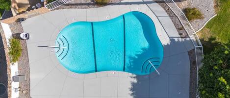 An aerial view of a swimming pool with a surrounding deck, lounge chairs, and a fenced area.