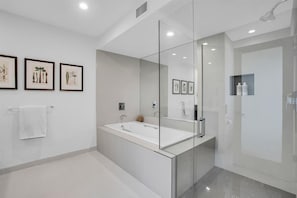 Ein modernes Badezimmer mit einer großzügigen, gläsernen Duschkabine, einer freistehenden Badewanne und botanischen Kunstwerken in Rahmen an der Wand.