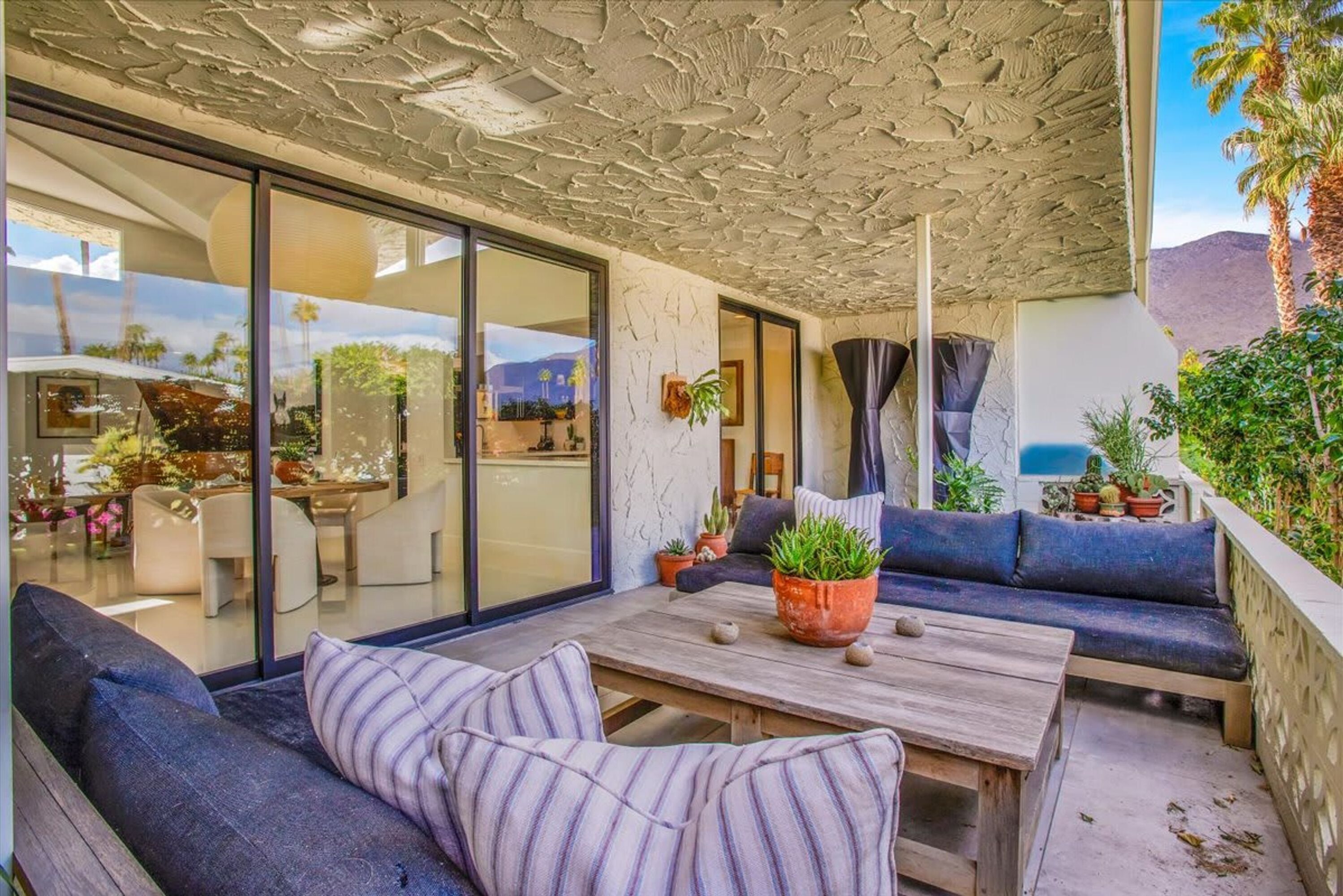 A modern outdoor living area with a wooden table, blue cushioned seating, and potted plants.