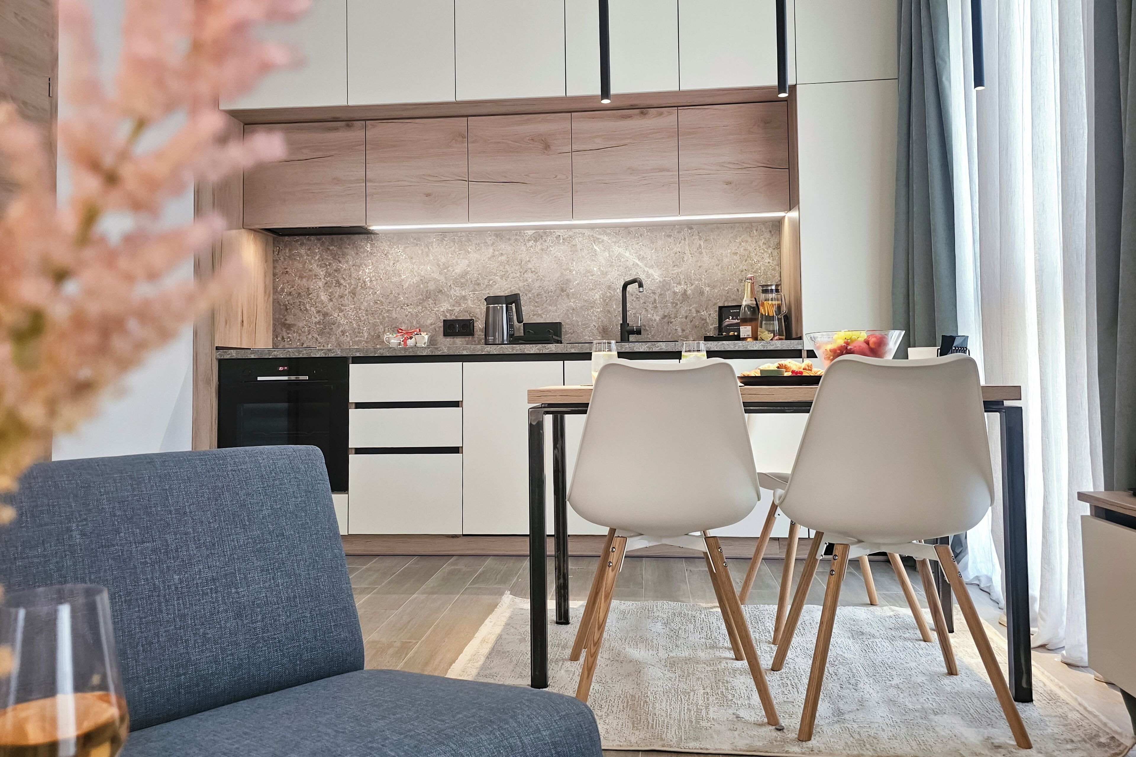 A modern kitchen with a dining area, featuring a sofa, two chairs, a coffee table, and a glass of wine.