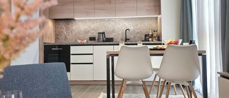A modern kitchen with a dining area, featuring a sofa, two chairs, a coffee table, and a glass of wine.