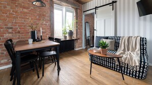 A cozy living room with a brick wall, wooden floor, a black and white patterned sofa, a dining table with chairs, and a potted plant. - Flatbook - In the Heart of Old Town (Gdansk)