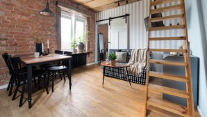 A cozy living room with a wooden dining table, black chairs, a black and white patterned sofa, a wooden ladder, and a brick wall. - Flatbook - In the Heart of Old Town (Gdansk)