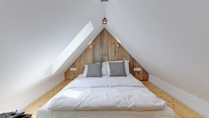 A bedroom with a sloped ceiling, wooden headboard, and two bedside lamps. - Flatbook - In the Heart of Old Town (Gdansk)