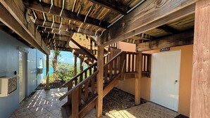 A wooden staircase leading to a room with a tiled floor, a door labeled A102, and a view of greenery outside.