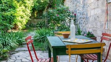 Ein Garten mit einer Terrasse, einem Tisch, Stühlen und einer Flasche.
