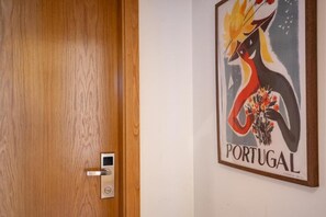 Une porte en bois, dotée d’une serrure moderne, et une affiche encadrée représentant un oiseau, le mot « PORTUGAL » étant inscrit sur le mur.