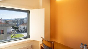 Ein Zimmer mit großem Fenster und Blick auf eine Stadtlandschaft, ein Holzstuhl und ein Tisch mit Wasserflaschen.