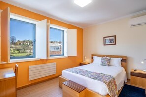 Une chambre à coucher avec un lit, des tables de chevet, un bureau et une fenêtre dont le volet est ouvert.