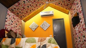 Una camera da letto con copriletto trapuntato, ventola a soffitto, condizionatore d'aria e due opere d'arte incorniciate appese al muro.