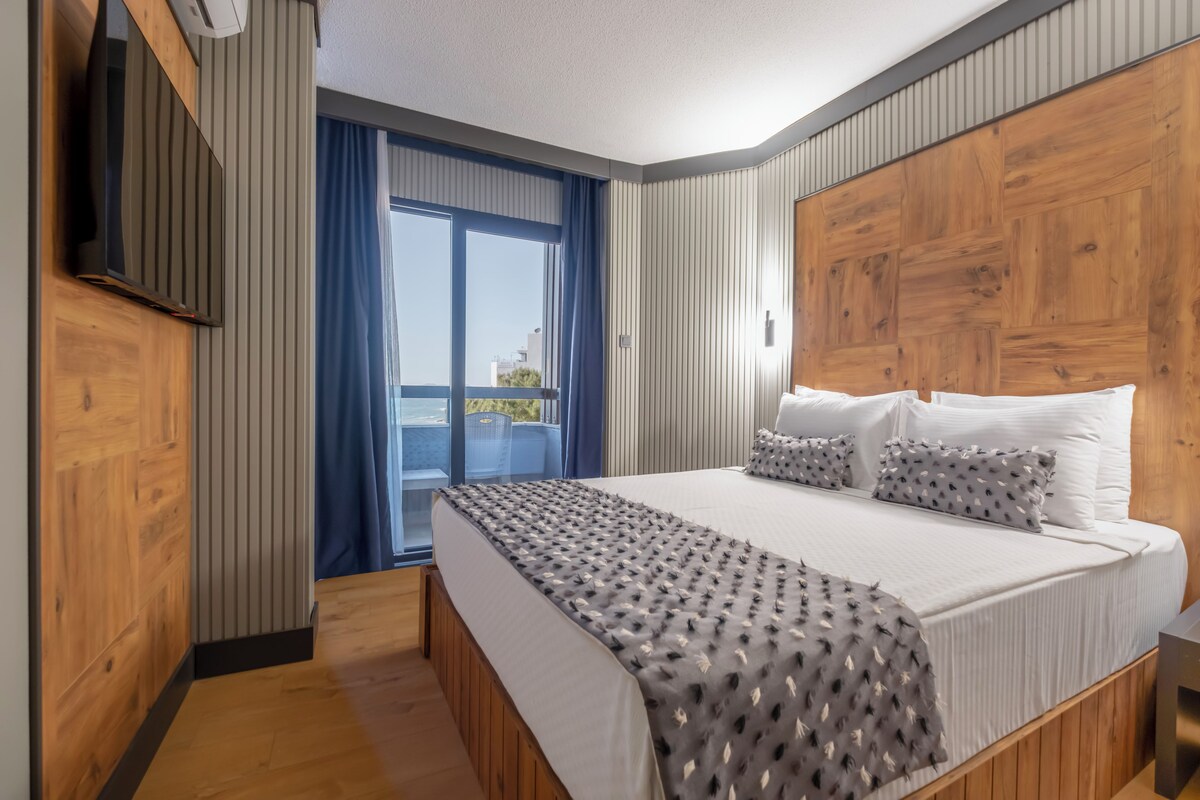 A hotel room with a large bed, a TV, a balcony with a view, and wooden paneling.