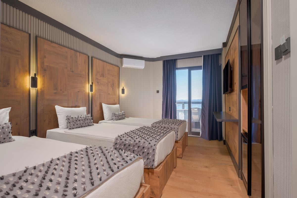Een hotelkamer met drie bedden, een televisie en een balkon met gordijnen.