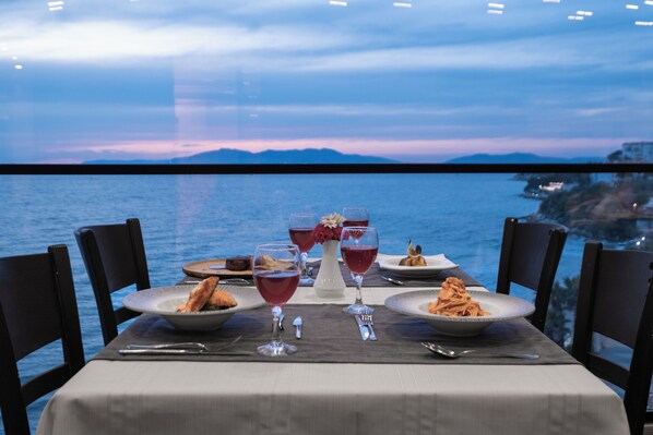 Une table dressée pour un repas, avec une vue sur la mer et les montagnes en arrière-plan.