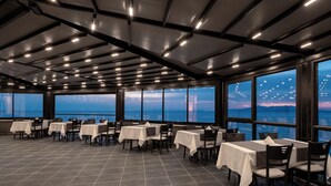 Un restaurant avec des tables et des chaises, de grandes fenêtres et une vue sur la mer.