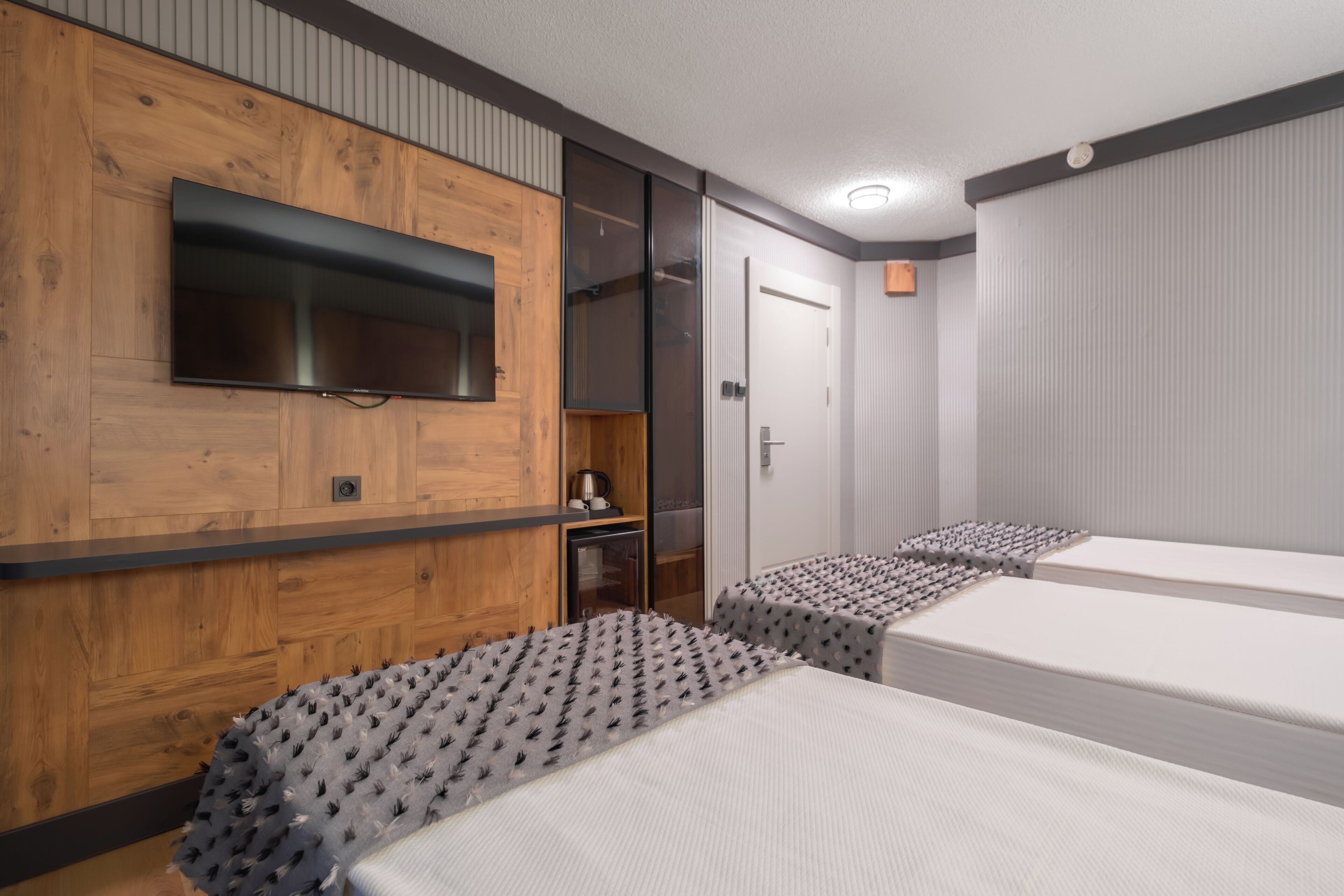 Ein Hotelzimmer mit Holzwand, Flachbildfernseher, Kleiderschrank, Bett mit gemustertem Überwurf und Nachttisch.