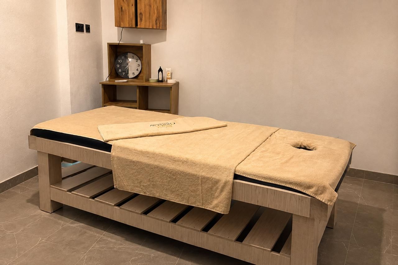 A massage table with a towel, wooden shelves, and a clock.