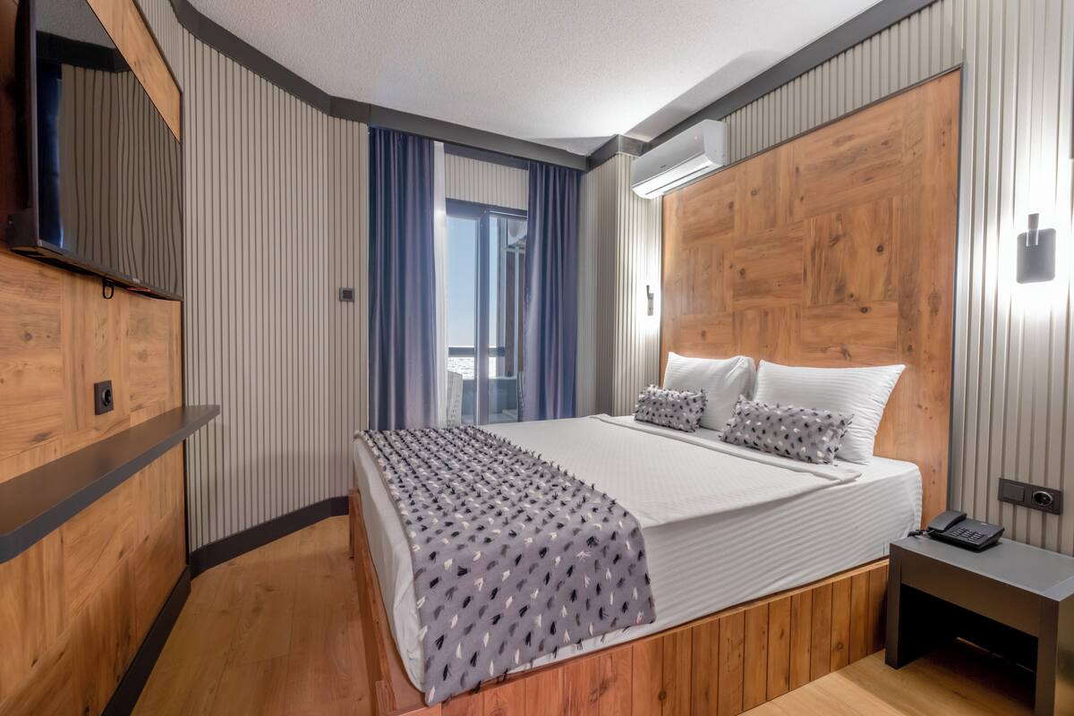 Een moderne hotelkamer met een groot bed, houten lambrisering, een ingebouwde televisie en een klein nachtkastje.