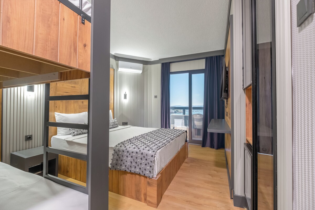 A modern hotel room with a bunk bed, a balcony with a view, and a large window with curtains.