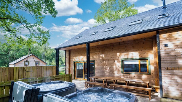 A wooden cabin with a covered patio, two hot tubs, and a wooden deck.