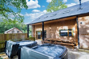 Una cabaña de madera con un porche techado, dos jacuzzis y una terraza de madera.