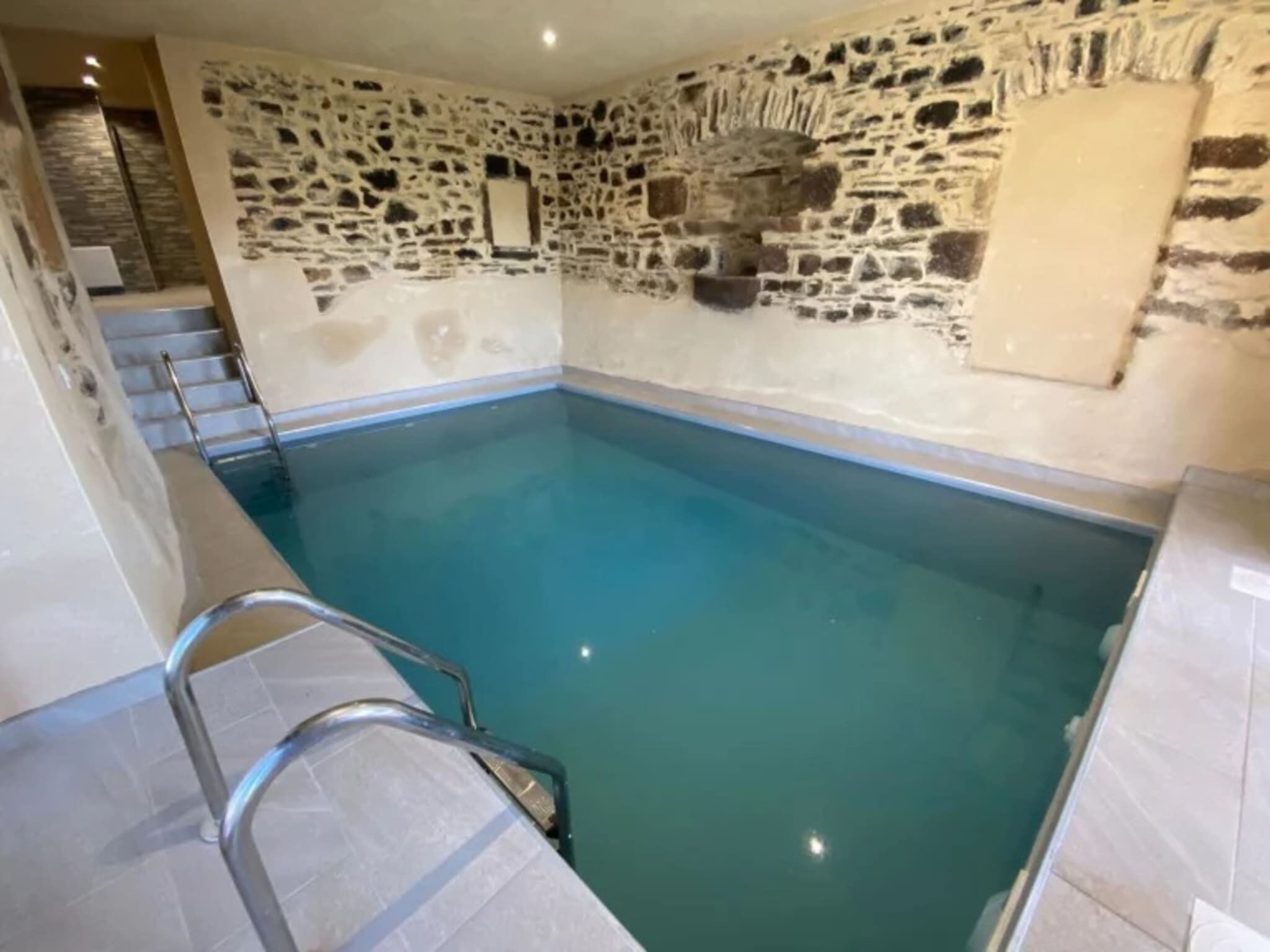 An indoor swimming pool with stone walls and a metal ladder.