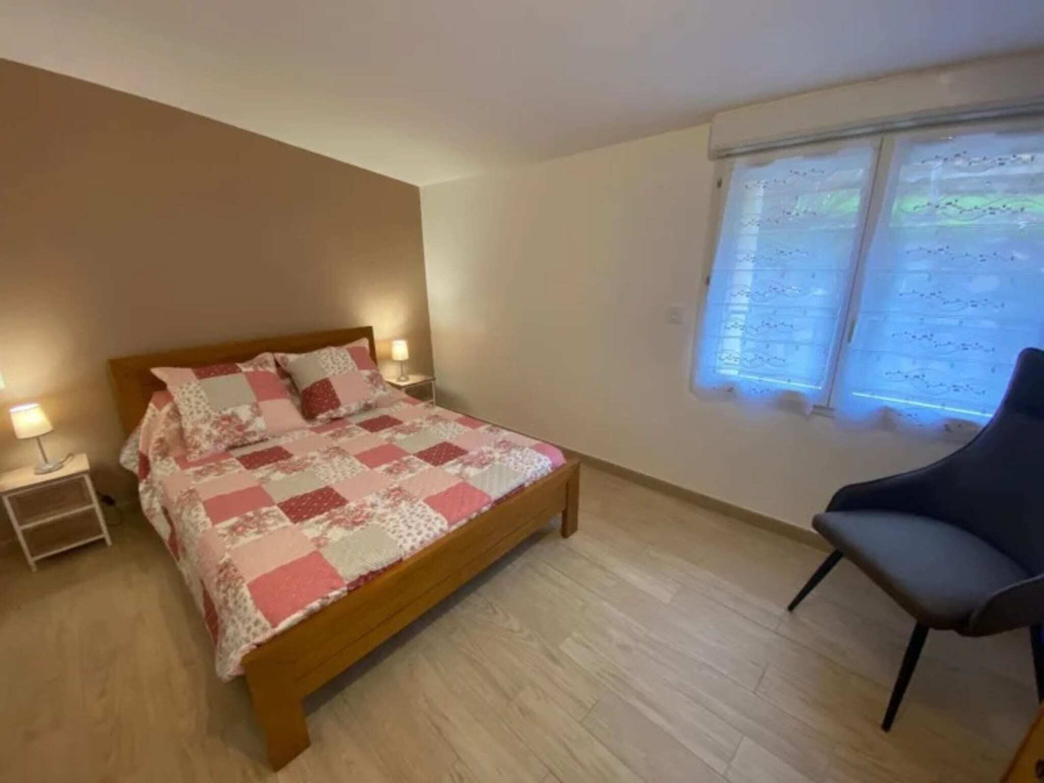 Un dormitorio con cama de madera, mesita de noche, una silla y ventana con persianas.