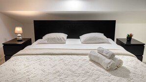 Een net opgemaakt bed met witte lakens en kussens, een bedlampje en een kleine plant in een potje op het nachtkastje.