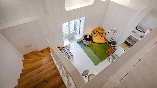 Een modern interieur met een houten trap, een zithoekje met een geel kussen, en een keuken.