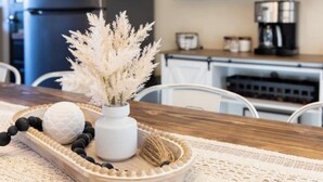 A dining table with a decorative centerpiece, a white vase with pampas grass, a white textured sphere, and a wooden tray with black and white beads. - High Street Hideaway (Athol)
