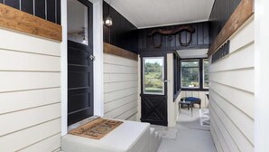 A narrow hallway with white and black siding, a bench with a welcome mat, and a door leading to a patio area with outdoor furniture. - High Street Hideaway (Athol)