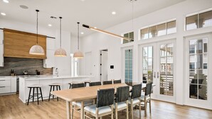 Une cuisine moderne avec un îlot central en bois, des luminaires suspendus et une grande table à manger entourée de chaises.