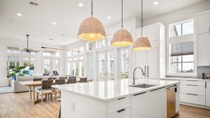 Une cuisine moderne avec des meubles blancs, un grand îlot central doté d’un évier et des luminaires suspendus.
